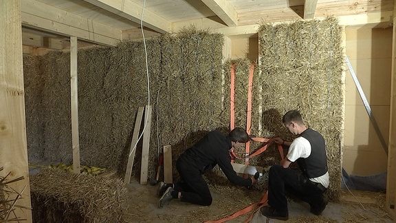 Männer arbeiten an einer Wand aus Strohballen. 