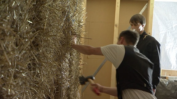 Männer arbeiten an einer Wand aus Strohballen. 