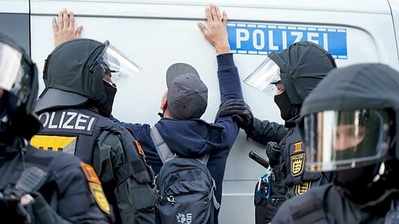 Ein Mann steht am 3. Juni mit erhobenen Händen auf einem Platz in Leipzig. Polizisten stehen davor, einer hält den Demonstrationsteilnehmer fest.