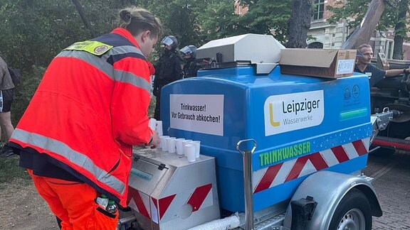 ein mitarbeiter der stadt Leipzig schiebt einen Wasserwagen, aus dem Trinkwasser an eingekesselte Bürger verteilt wird am Abend des 3.6.2023.