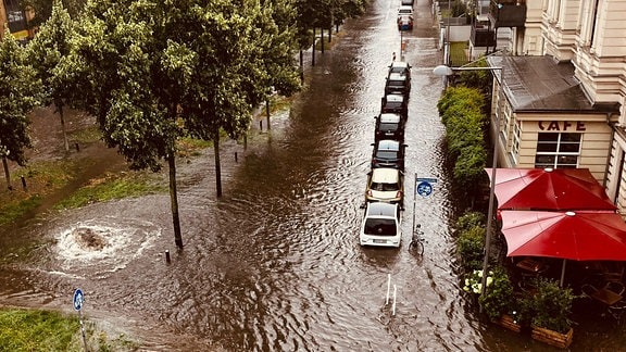 Eine überflutete Straße. Das Wasser geht bis an die Häuser und Grnflächen und Parkplätze sind überschwemmt.