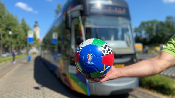 Ein Ball wird vor eine Straßenbahn gehalten