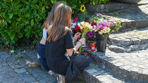 Zwei Mädchen legen Blumen nieder. 