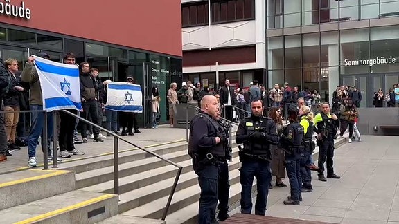 Menschen mit Israelfahnen und Einsatzkräfte der Poliezi stehen vor einem Gebäude.