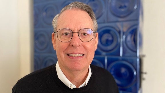 Ein Mann mit Brille und grauen Haaren lächelt in die Kamera.