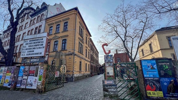 Blick auf eine Einfahrt mit Plakaten und einer großen Tafel, die Veranstaltungen ankündigt; darunter steht "Werk 2".