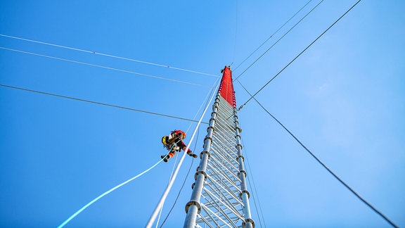 Ein Mann klettert auf einem 300 Meter hohen Windmast.  