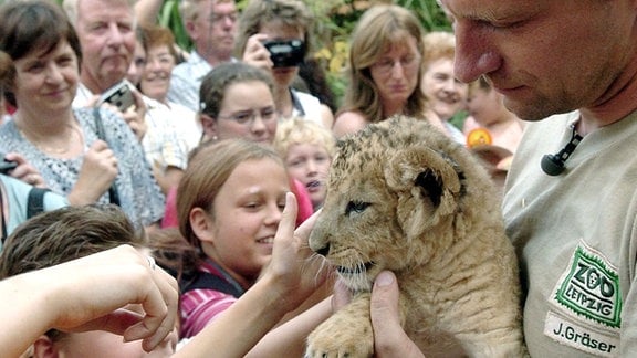 Der Tierpfleger Jörg Gräser (r) zeigt Besuchern das am 02. Juli 2004 im Leipziger Zoo geborene Löwenbaby, das am gleichen Tag auf den Namen "Malik" getauft wurde. 