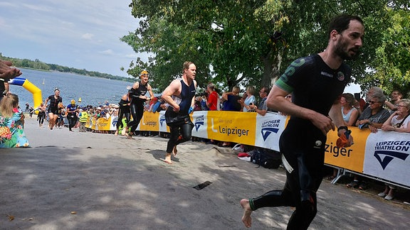 Menschen rennen vom See hoch zu ihren Rädern beim 40. Leipziger Triathlon.