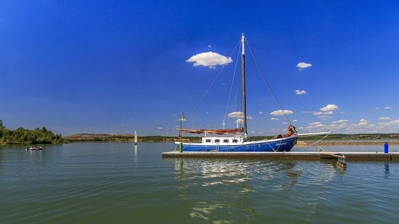 Ein Segelboot mit gerefften Segeln am Steg in einem See.