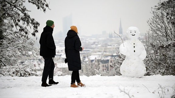 Zwei Spaziergänger am Fockeberg wandern an einem Schneemann vorbei. 