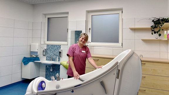 Eine Frau mit rose Kittel steht in einem gefliesten Raum mit Badewanne