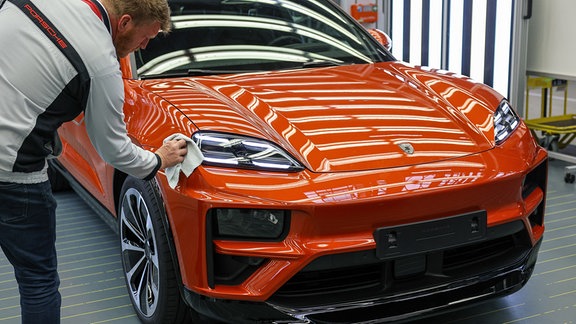 Ein Porsche-Mitarbeiter prüft in der Qualitätskontrolle einen vollelektrischen Porsche Macan im Werk Leipzig.