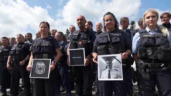 Bundespolizisten stehen geschlossen am Grenzübergang und halten Gedenkbilder. 