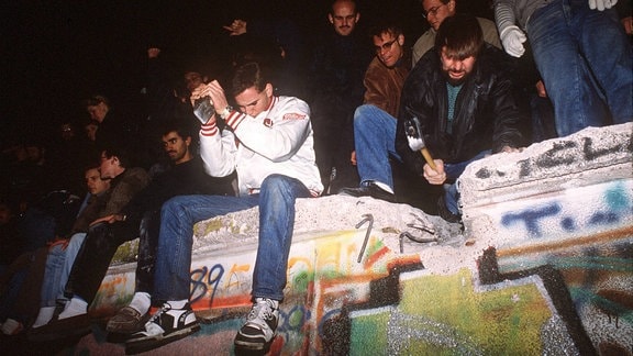  Junge Männer hämmern auf die Berliner Mauer ein.