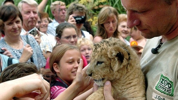 Der Tierpfleger Jörg Gräser (r) zeigt Besuchern das am 02. Juli 2004 im Leipziger Zoo geborene Löwenbaby, das am gleichen Tag auf den Namen "Malik" getauft wurde.