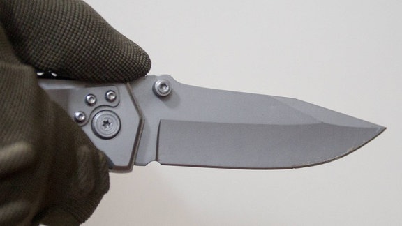 Person hält vor einem neutralen Hintergrund ein Messer in der Hand mit Handschuh