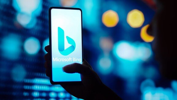 Eine Hand hält ein Sm,artphone auf dem das Logo von Microsoft Bing zu sehen ist.