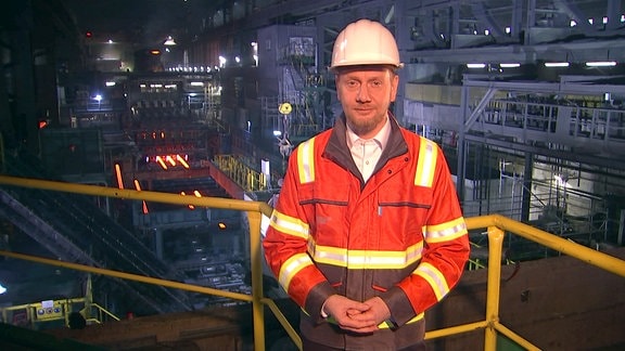 Ministerpräsident Kretschmar mit Helm und Arbeitskleidung in einer Fabrikhalle
