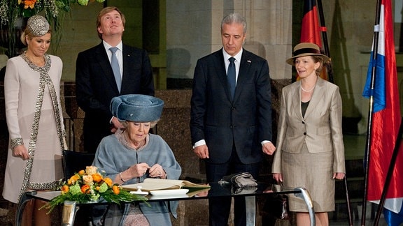 Königin Beatrix der Niederlande trägt sich am Donnerstag (14.04.2011) in der Staatskanzlei in Dresden in das Goldene Gästebuch der Stadt ein, während im Hintergrund Prinzessin Maxima, Prinz Willem-Alexander, Sachsens Ministerpräsident Stanislaw Tillich (CDU) und dessen Ehefrau Veronika stehen. 