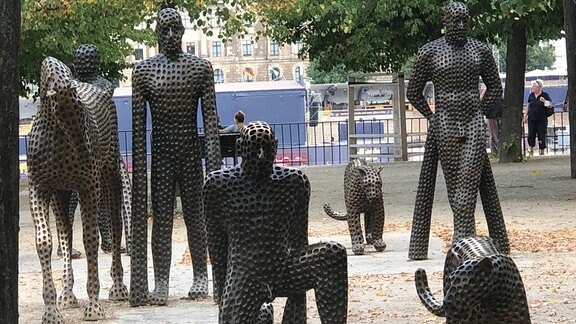 Bronzefigurengruppe bestehend aus Pferden, Raubkatzen und Menschen mit viel zu langen Armen.