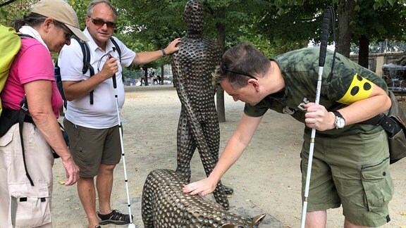 Um eine der Raubkatzen aus dem Werk "Mission" von Michal Gabriel stehen die Besucher der Führung. Daniel Martin erkundet die Oberfläche mit der Hand.