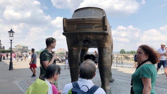 Lydia Hänsel steht mit ihrer Besuchergruppe vor dem Werk "QUO VADIS?" (1990) von David Černý: Einem betont männlichem Trabant auf riesigen Füßen, statt Rädern.