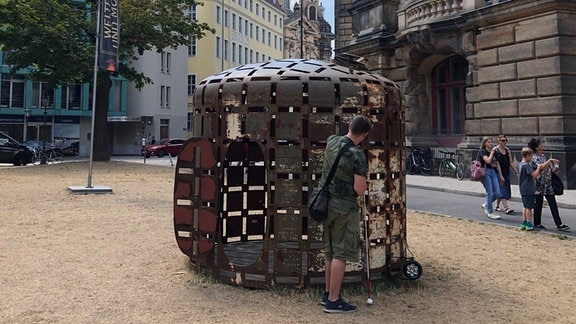 Daniel Martin steht vor einem der Getreidesilos des Werkes OPUŠTENÁ OBYDLI von dem Künstler Čestmír Suška. Im Hintergrund ist die Frauenkirche zu sehen.