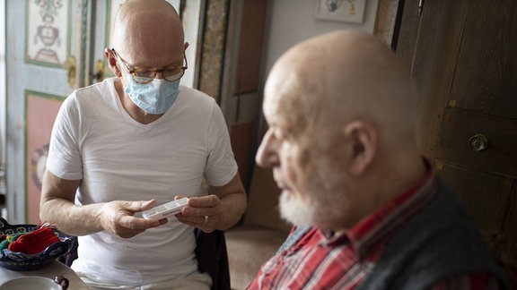 Ein Altenpfleger kontrolliert die Medikamenten Einnahme eines älteren Mannes.