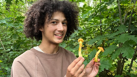 Ein junger Mann hält zwei helle Pilze in der Hand