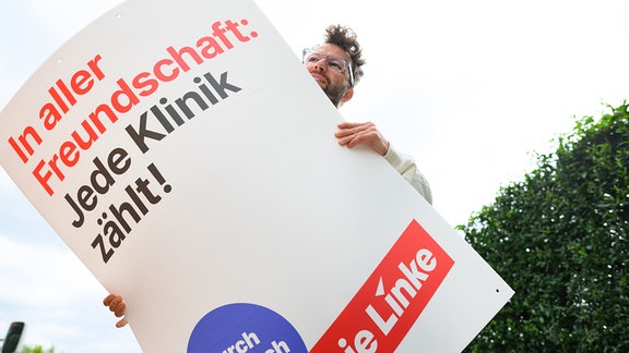 Lars Kleba, Geschäftsführer der Linken in Sachsen, hält ein Wahlplakat zur Landtagswahl in Sachsen mit der Aufschrift „In aller Freundschaft: Jede Klinik zählt!“ in den Händen. 