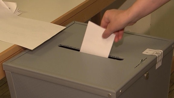 Ein Stimmzettel wird in eine Wahlurna geworfen.