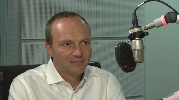 Ein Mann sitzt hinter einem Mikrofon in einem Radio-Studio
