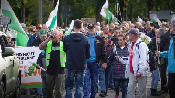 Demonstranten laufen auf einer Straße und halten Flaggen des Königreichs Sachsen.