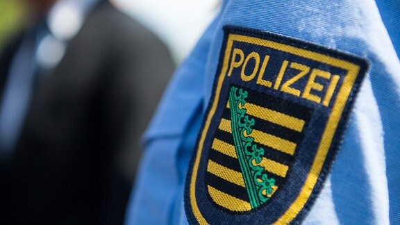 Logo der sächsischen Polizei ist an einem Polizeiuniform angebracht.