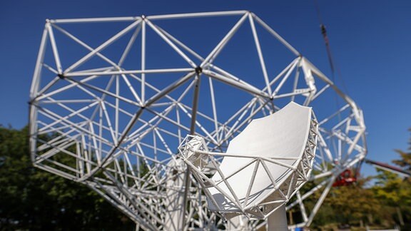 Das Modell einer 18 Meter großen Parabolantenne als Bestandteil des künftig größten Radioteleskopes der Welt steht vor dem im Bau befindlichen Prototypen auf dem Gelände der mtex antenna technology GmbH. 