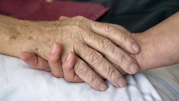 Die Hand einer Pflegerin haelt die Hand eines alten Mannes.