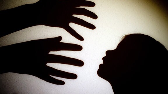 Schatten von Händen einer erwachsenen Person und dem Kopf eines Kindes sind an einer Wand zu sehen