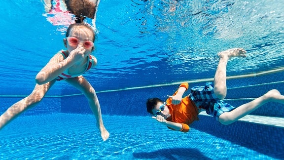 Zwei Kinder tauchen in einem Schwimmbecken, dazu der Schriftzug "Sommer, Sonne, Badespaß"