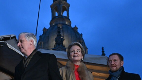 König Philippe und Königin Mathilde der Belgier gehen mit Michael Kretschmer (CDU), Ministerpräsident von Sachsen, über den Weihnachtsmarkt auf dem Neumarkt vor der Frauenkirche.