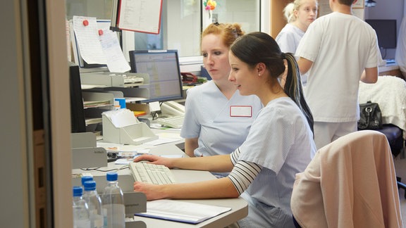 Schwestern und Pfleger auf einer Stationen in der Pflege arbeiten am Schreibtisch