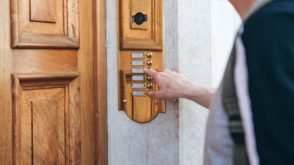 Ein Mensch klingelt vor einer Haustür an einer Gegensprechanlage