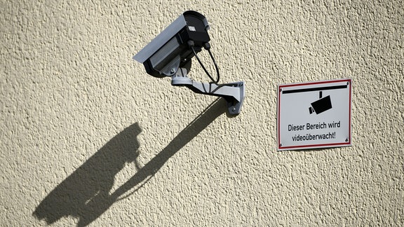  Eine Ueberwachungskamera haengt mit einem Warnschild an der Wand eines Wohnhauses.