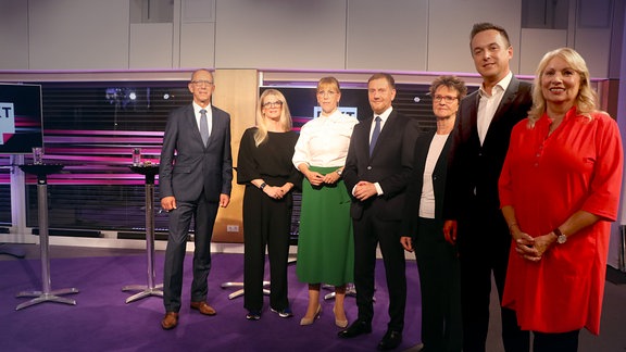 Sieben Männer und Frauen stehen in einem Studio. 