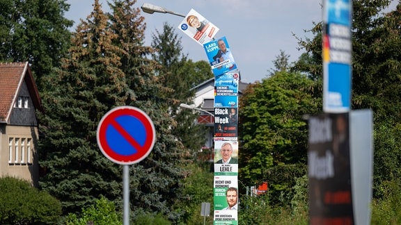 Sechs Wahlplakate von CDU, AfD und Linkspartei und ein Werbeplakat umhüllen einen Laternenmast.