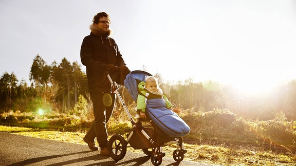 Mann geht mit Kind im Kinderwagen spazieren