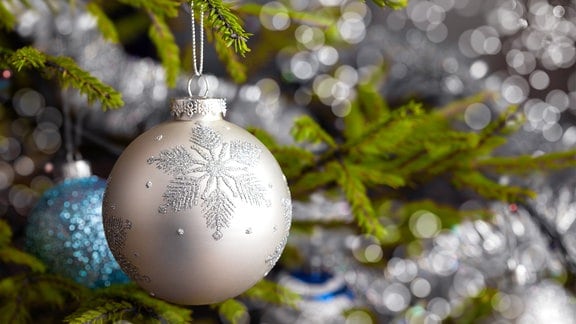 Eine silberfarbene Weihnachtskugel in Tannenzweigen.