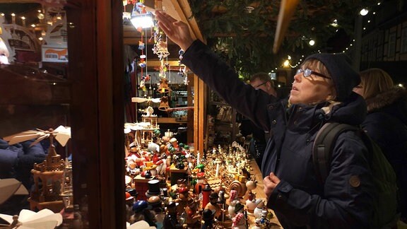 Eine Frau schaut sich an einem Weihnachtsmarktstand mit Holzfiguren Artikel an.