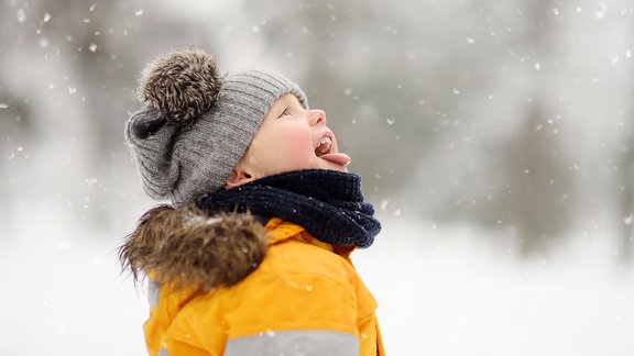 Ein Junge versucht mit seinem Mund Schneeflocken aufzunehmen.