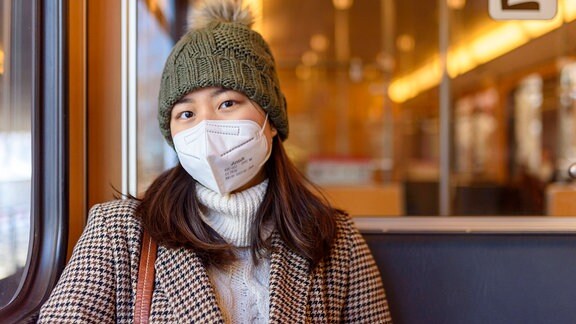 Eine Frau mit Maske und Wintermütze sitzt in einer Straßenbahn.